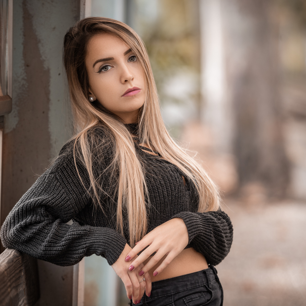 Красивая блондинка в вязаном свитере у стены 