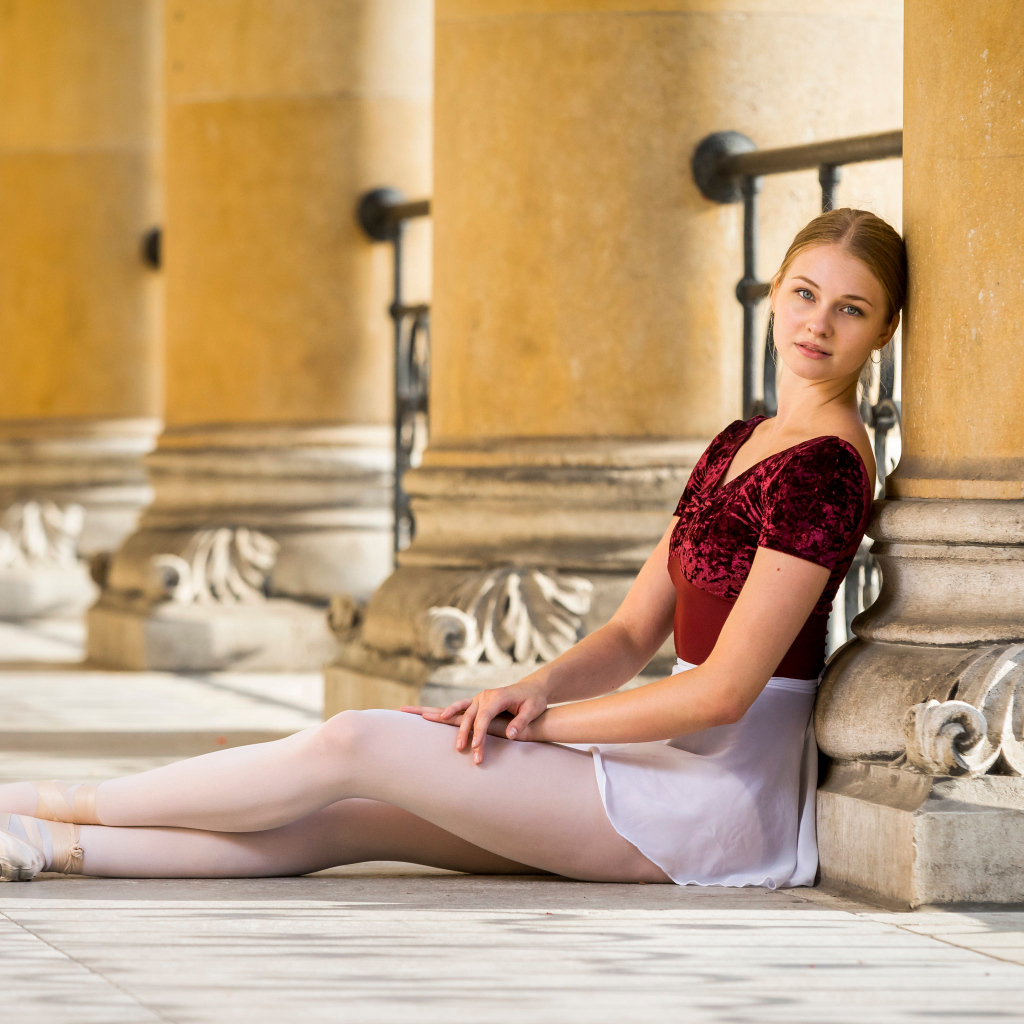 Красивая девушка балерина сидит на полу у колонны 