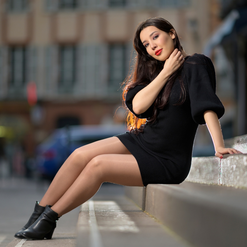 Красивая девушка в черном платье сидит на ступенях