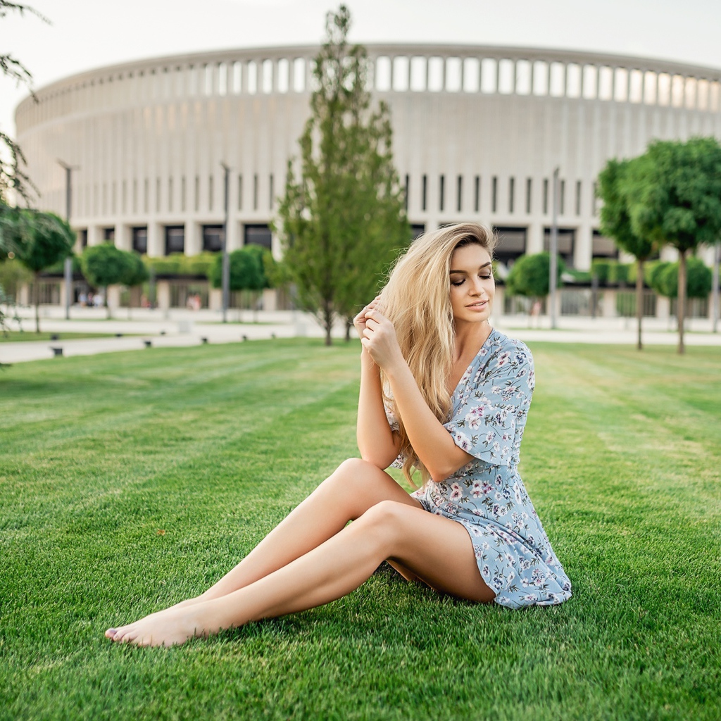 Красивая девушка в платье сидит на зеленом газоне 