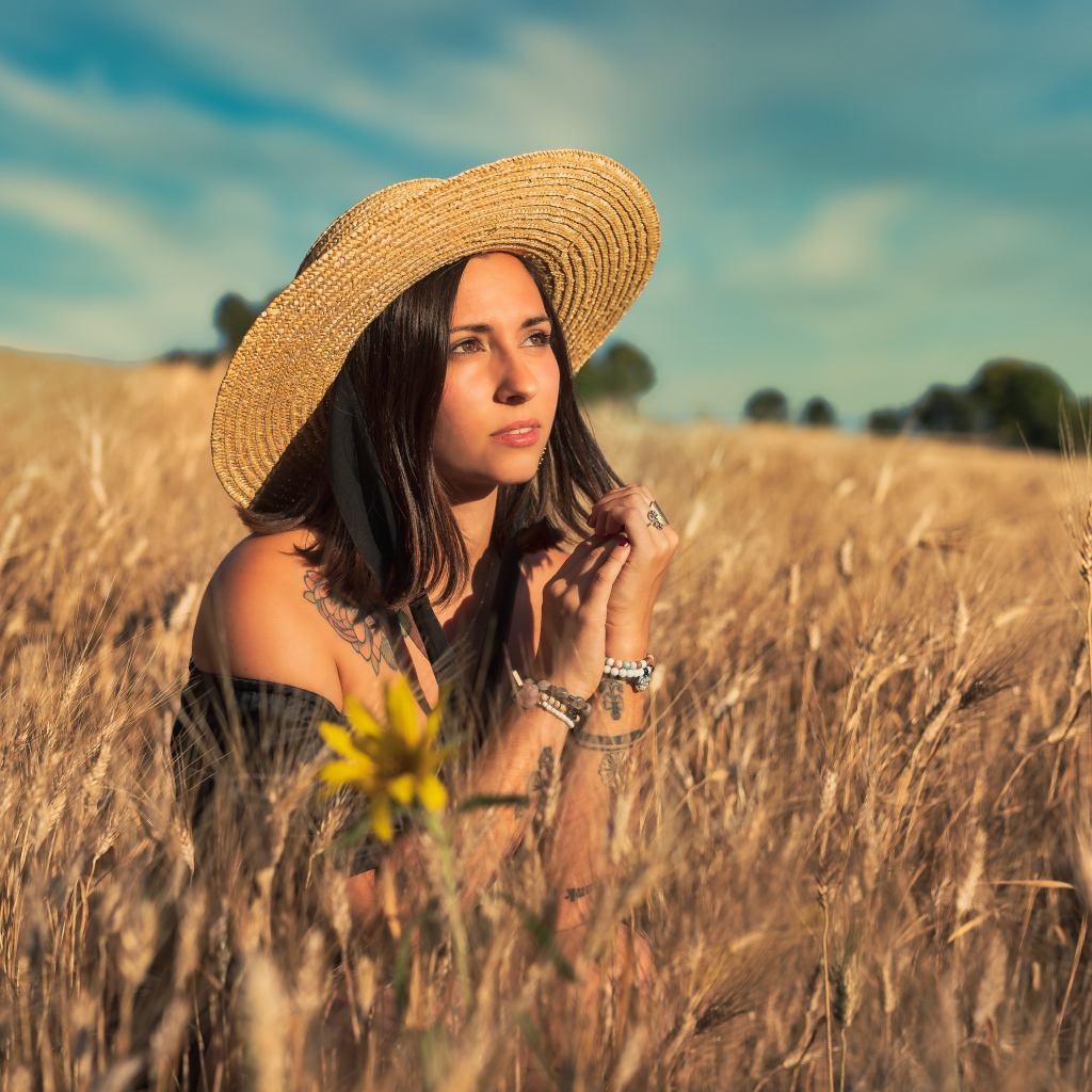 Красивая девушка в шляпе сидит на поле с пшеницей