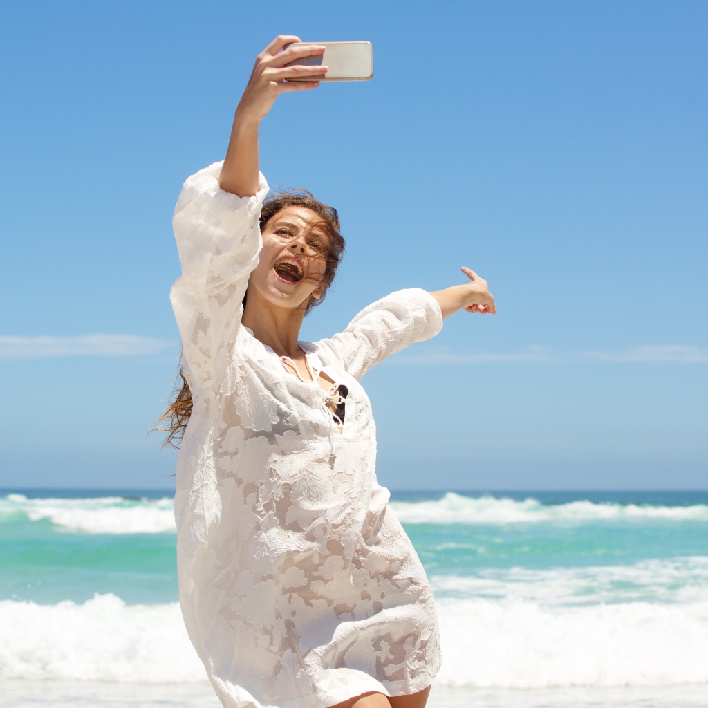 Красивая девушка в белом платье делает селфи на море 