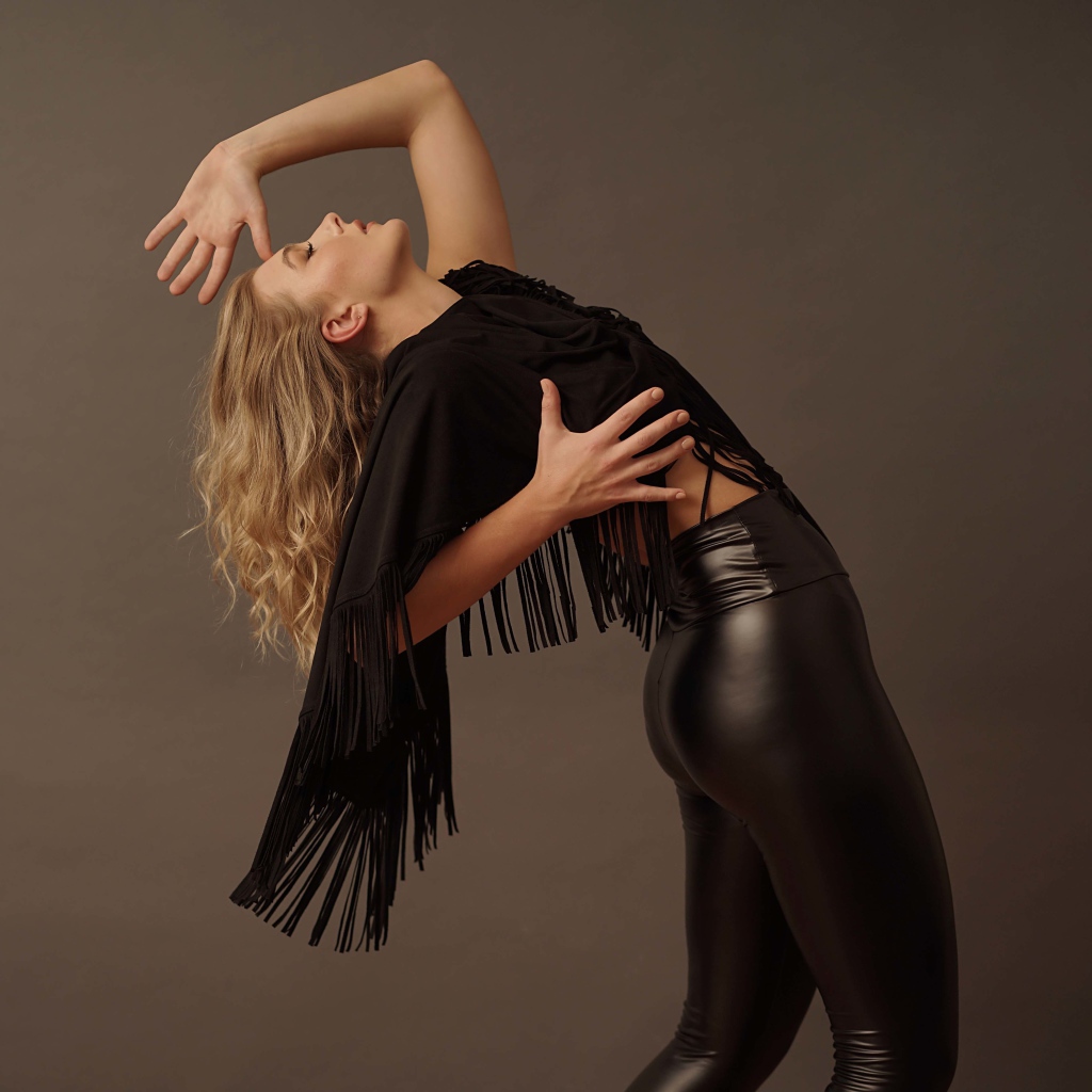 Красивая девушка в черных кожаных брюках на сером фоне