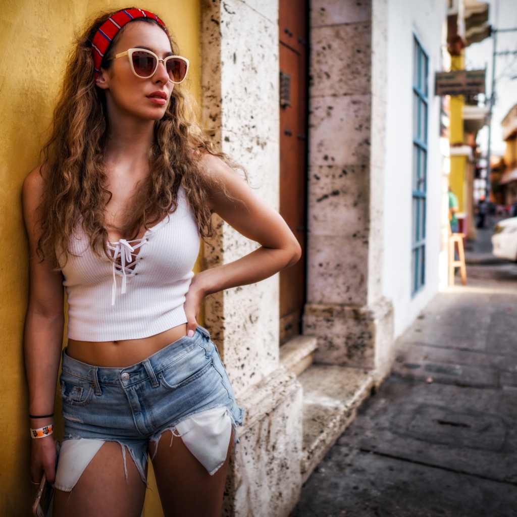 Красивая девушка в солнечных очках стоит у стены