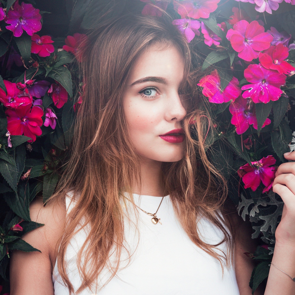 Красивая девушка стоит у зарослей с розовыми цветами