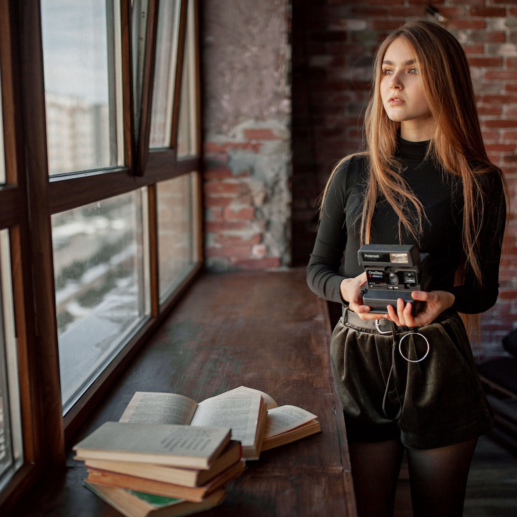 Красивая девушка с фотоаппаратом в руках у окна 