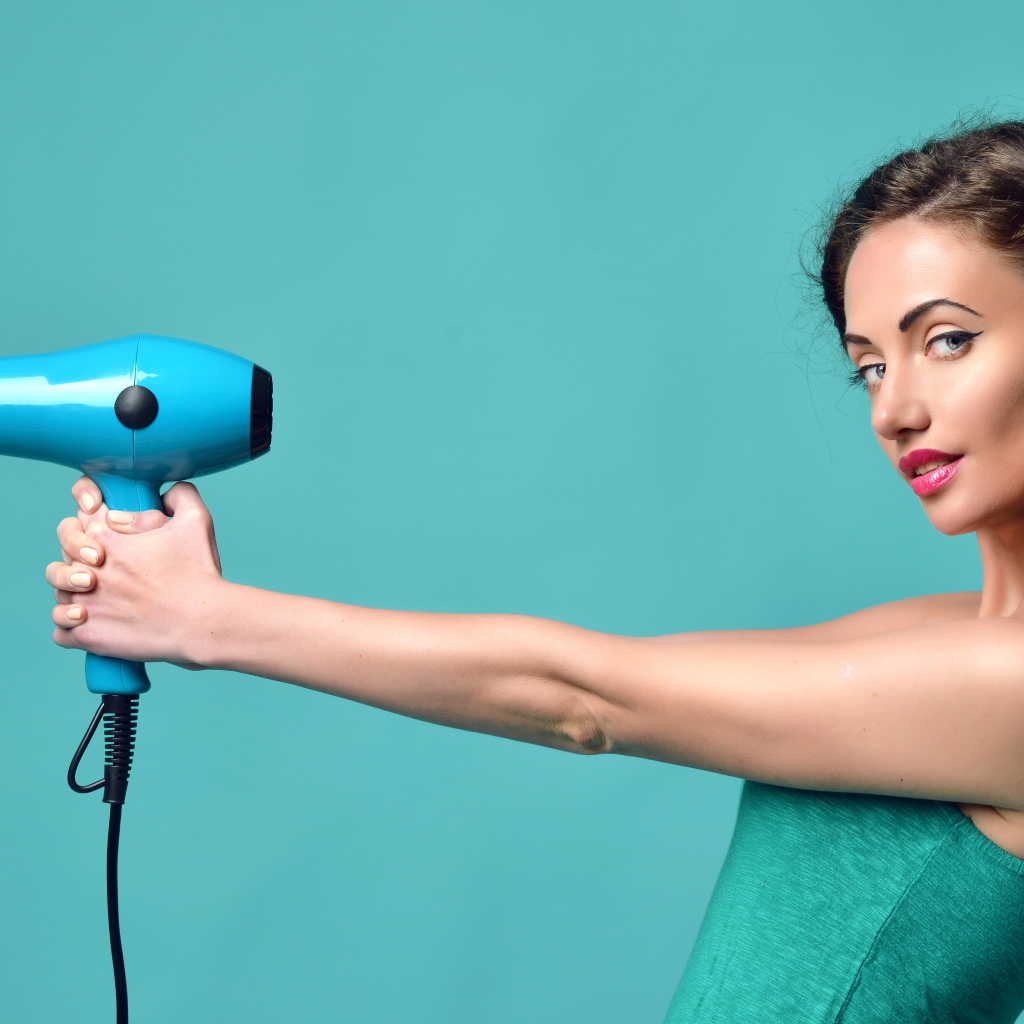 Красивая девушка с феном в руках на голубом фоне