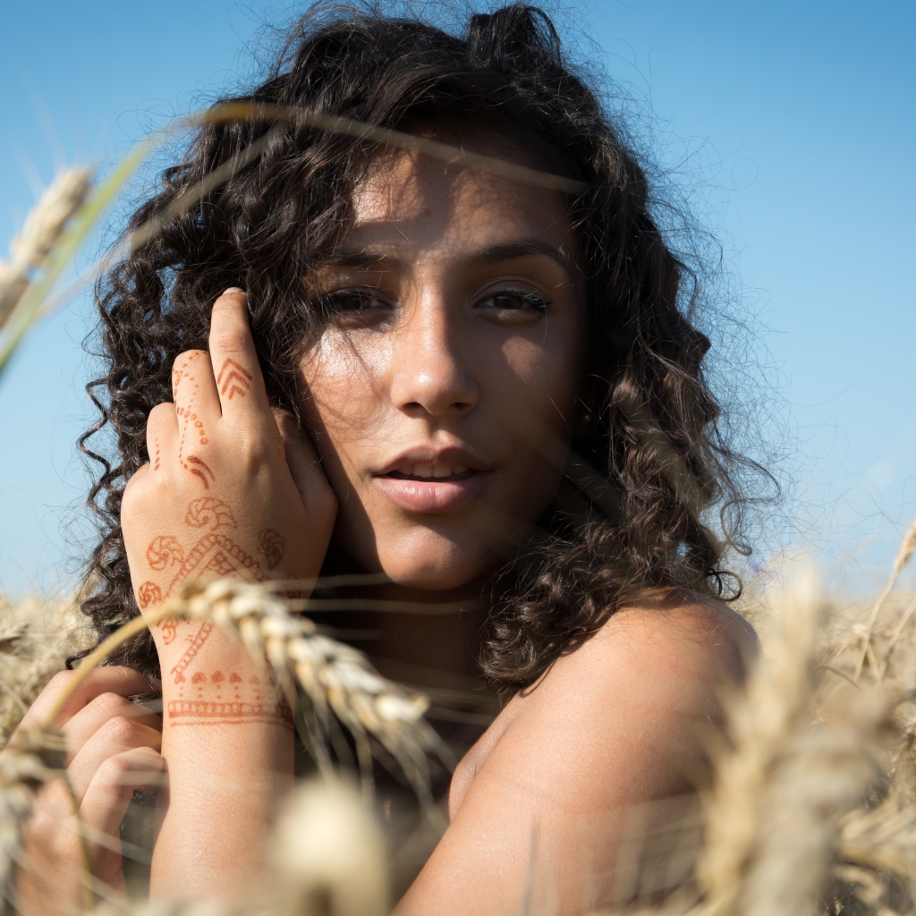 Красивая девушка с рисунком мехенди на руке на пшеничном поле 