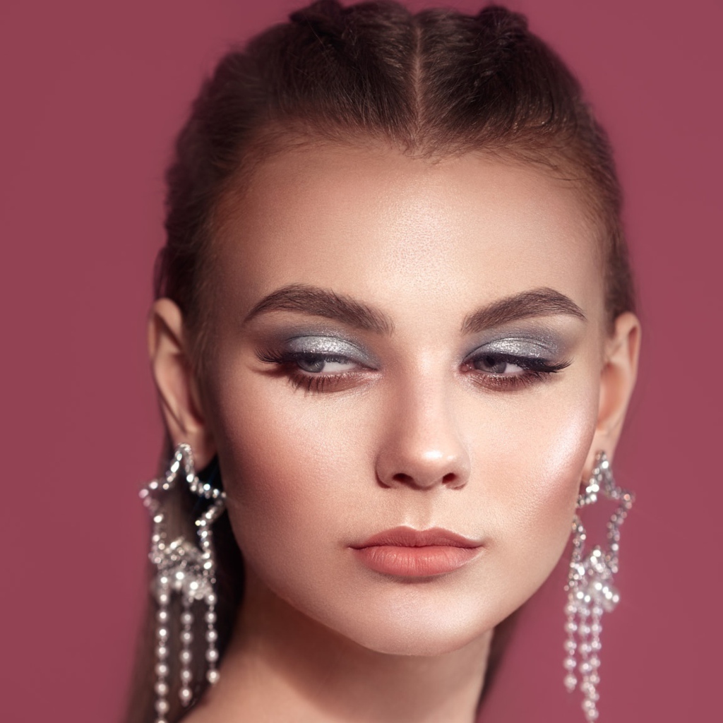 Красивая девушка с макияжем и большими серьгами на розовом фоне