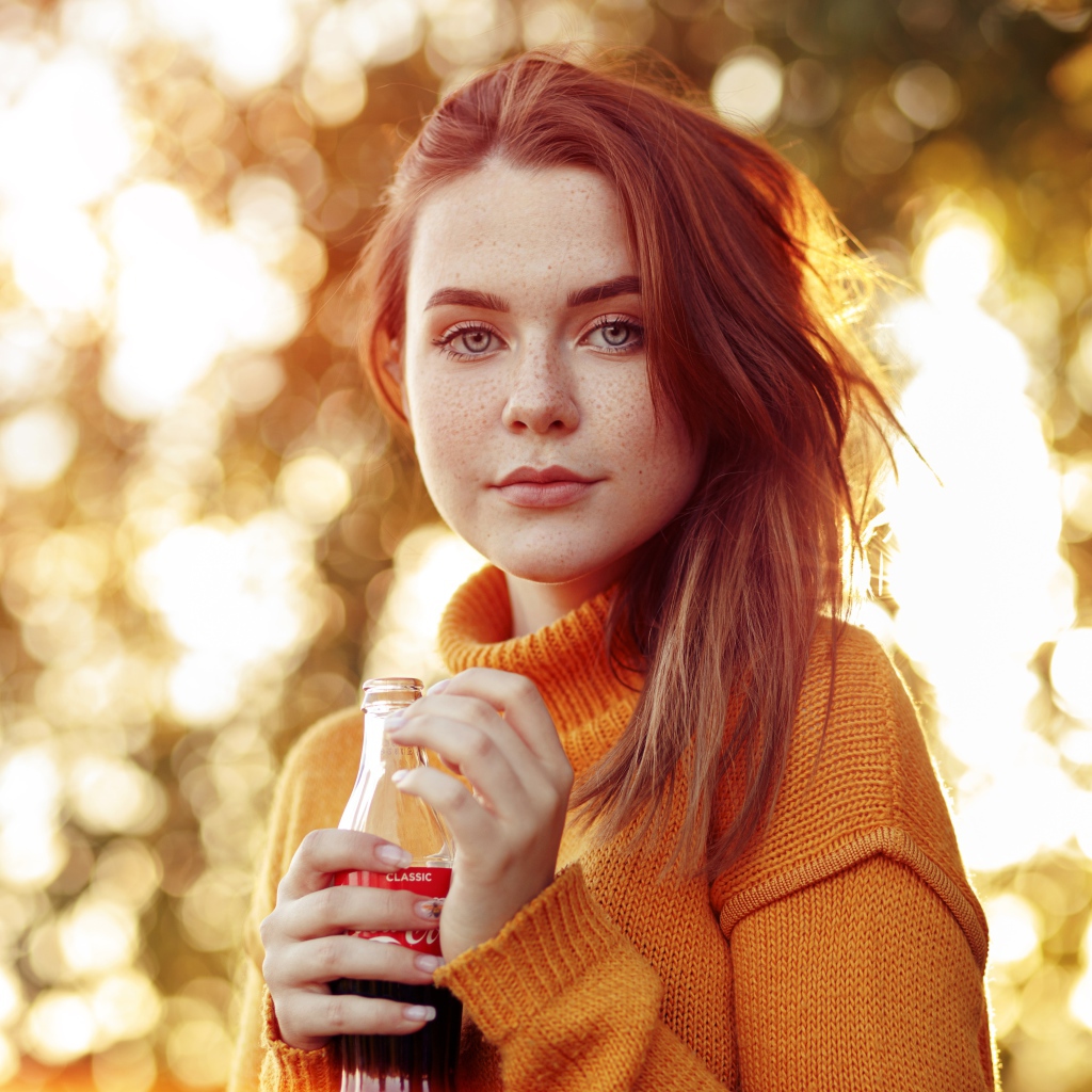 Красивая рыжеволосая девушка с бутылкой кока колы в руке 