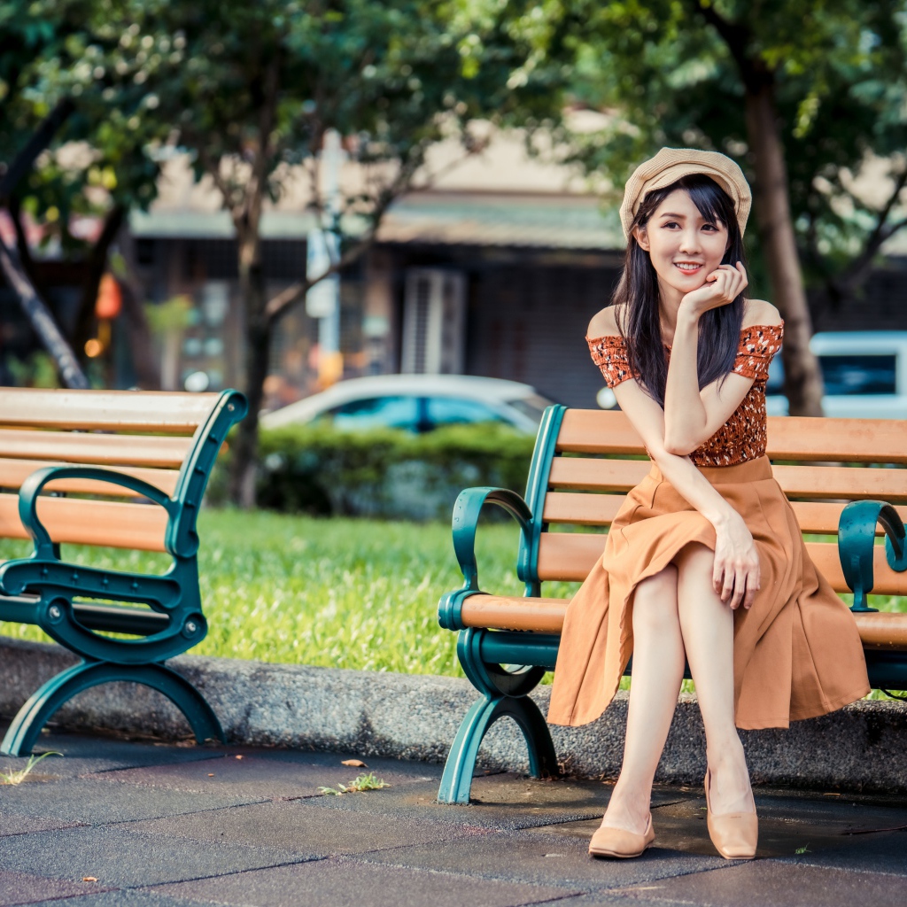 Красивая улыбающаяся азиатка сидит на лавке в парке