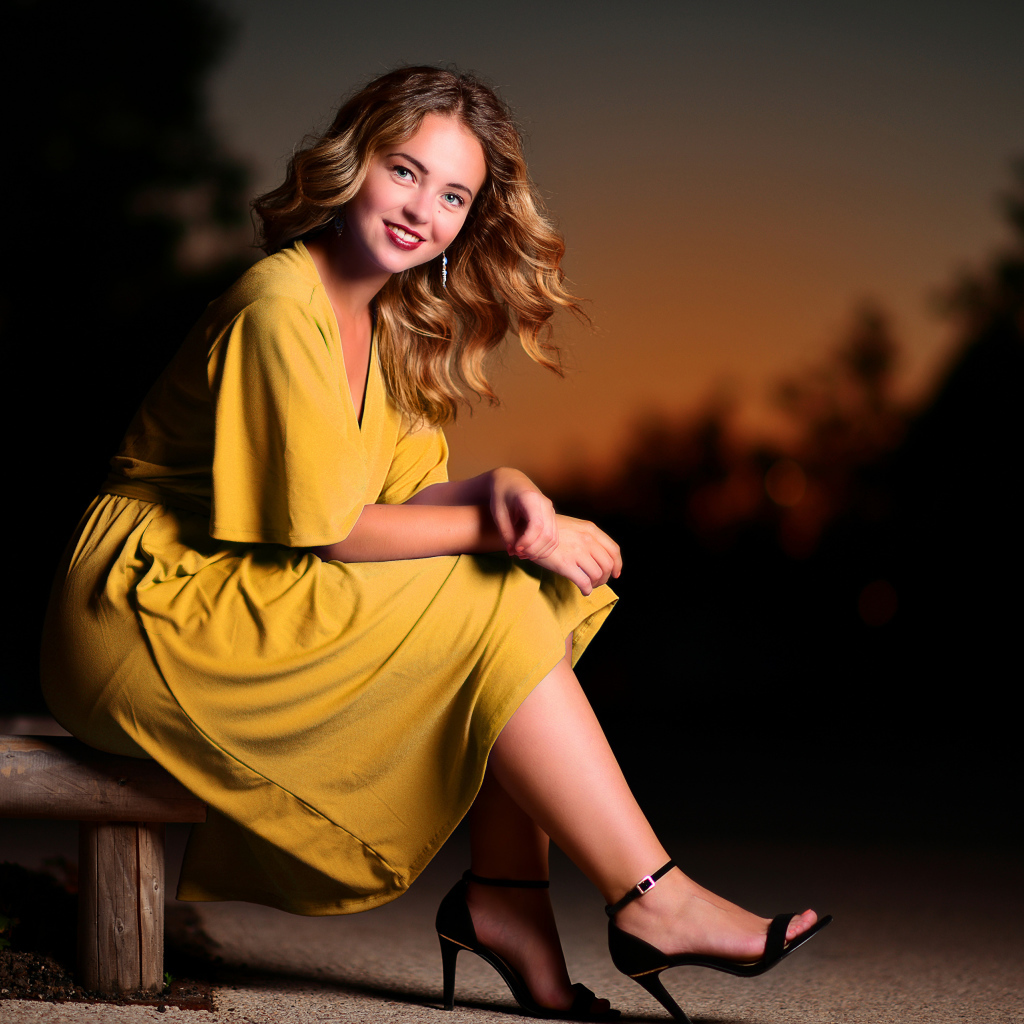 Красивая улыбающаяся девушка в желтом платье сидит на лавке 