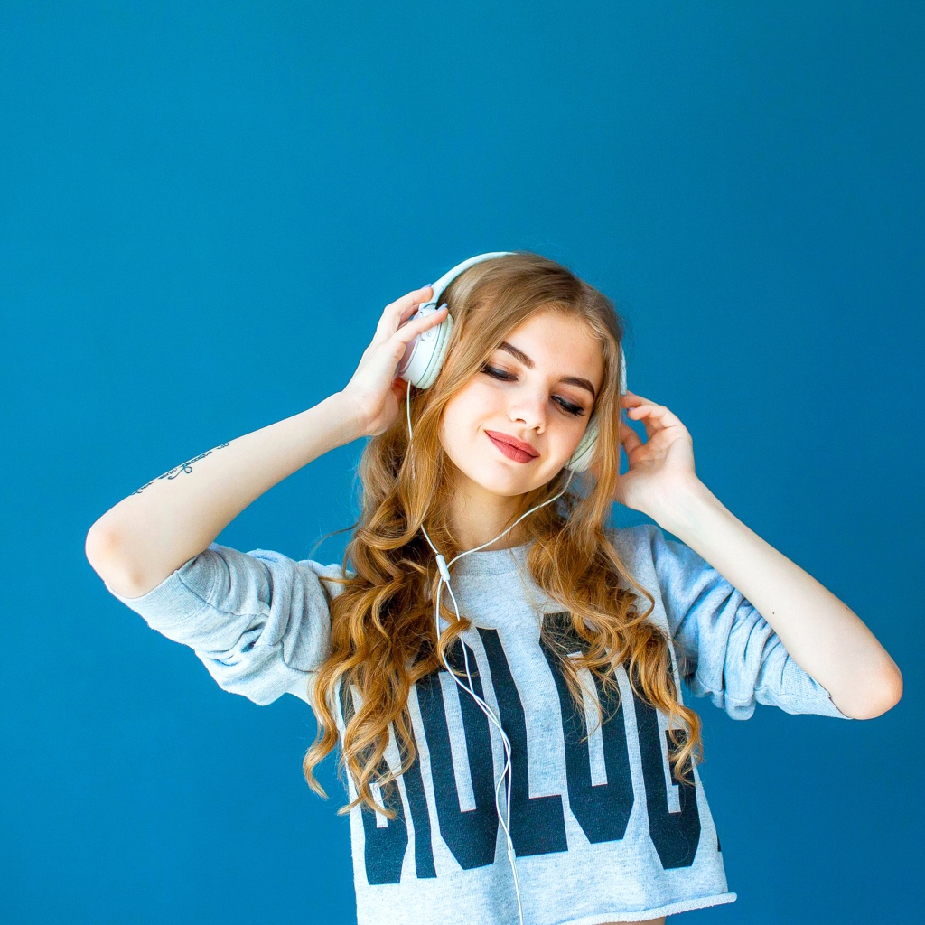 Красивая молодая девушка в наушниках на голубом фоне