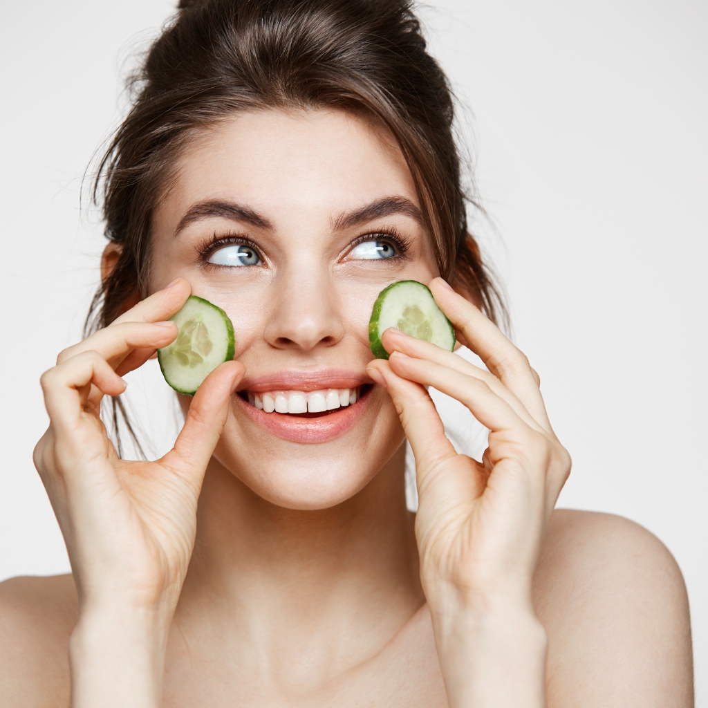 Голубоглазая девушка прикладывает огурцы к лицу 