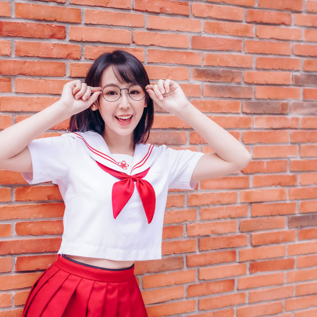 Яркая веселая азиатка в очках у кирпичной стены