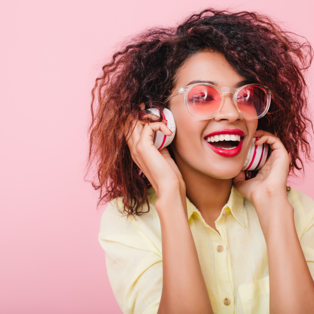 Яркая улыбающаяся девушка слушает музыку в наушниках 
