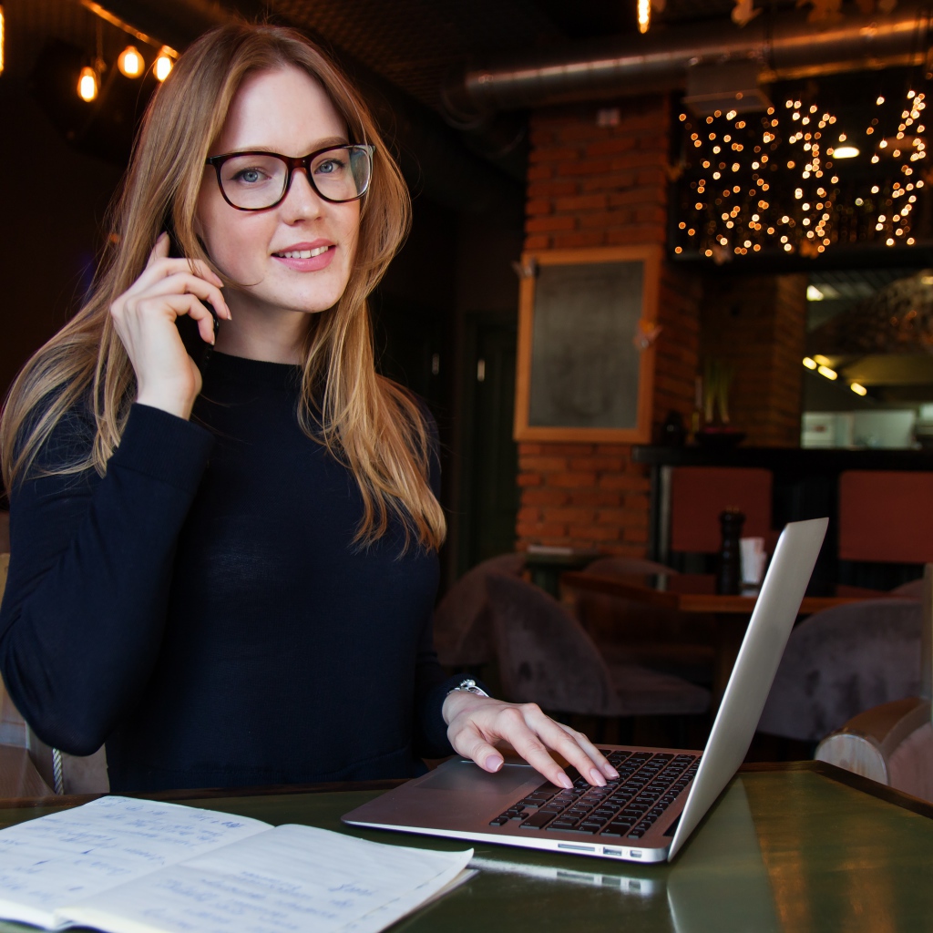 Деловая девушка в очках сидит с кафе с ноутбуком