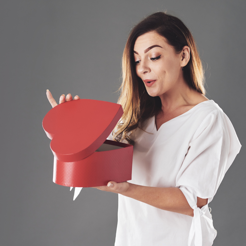 Любопытная девушка смотрит в красную коробку в форме сердца