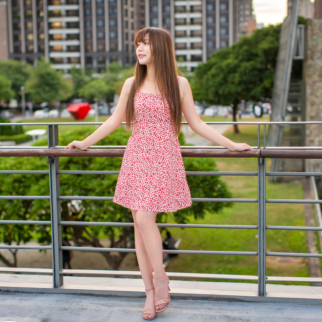 Милая девушка азиатка в платье стоит у перил 