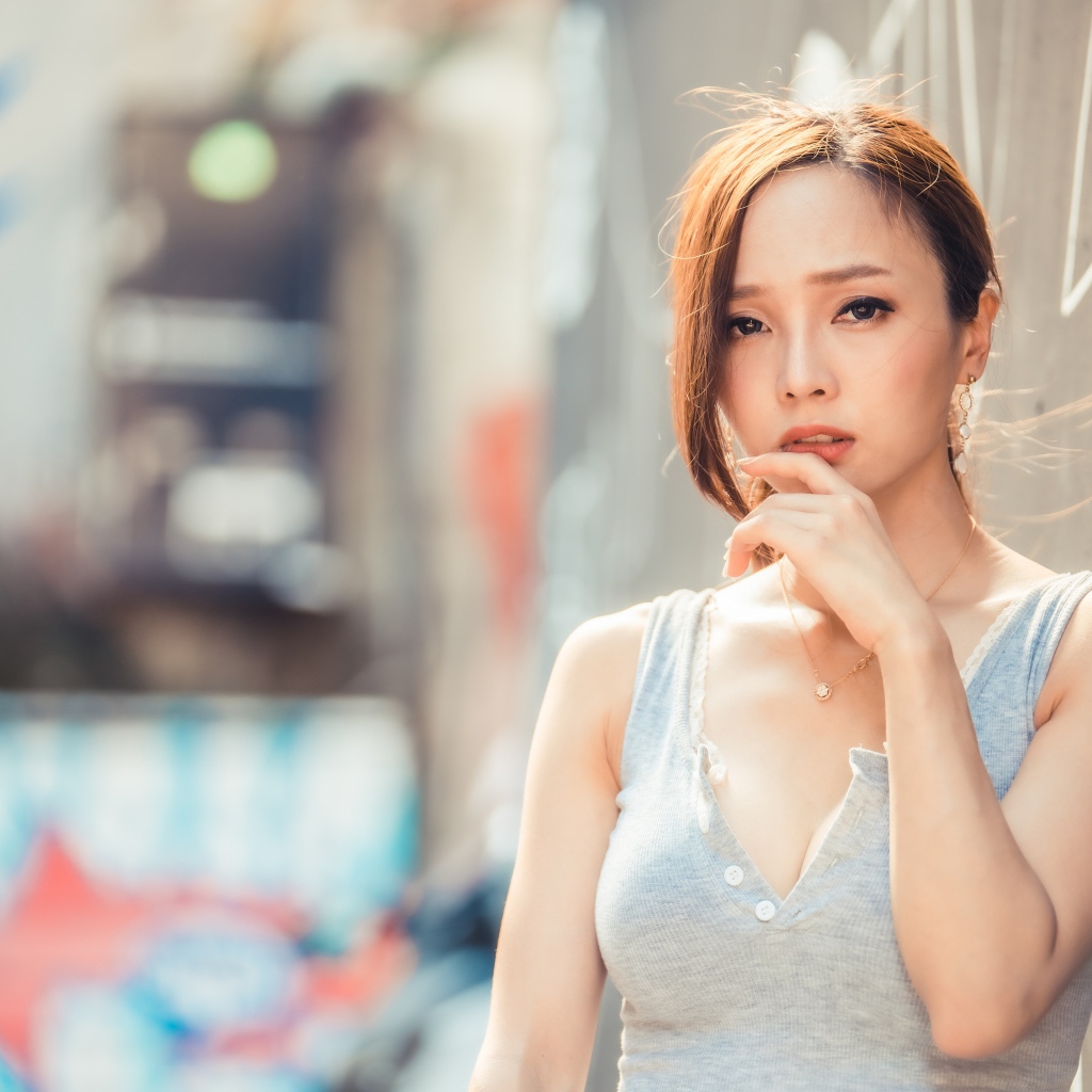 Милая девушка азиатка  с рукой у лица стоит у стены 