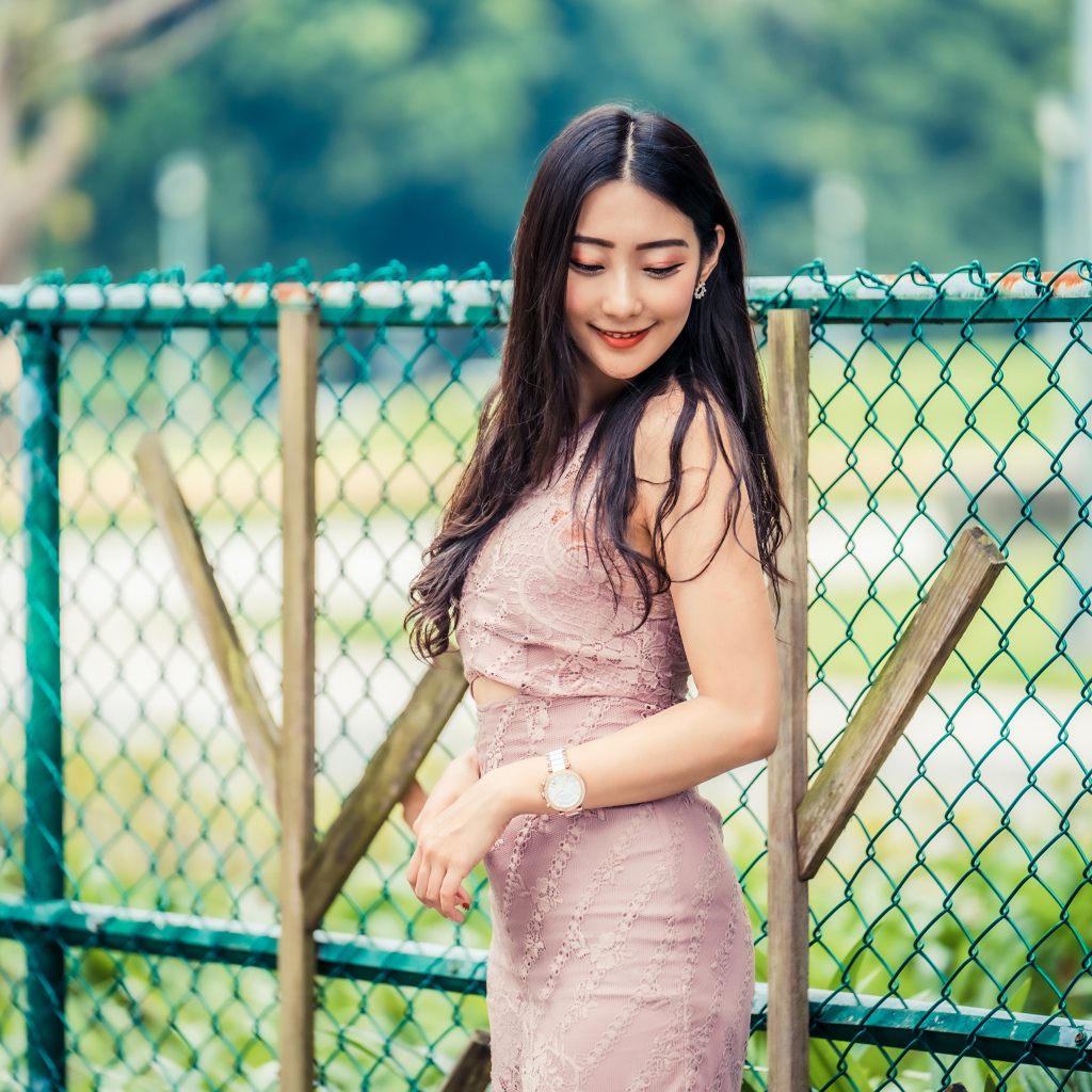 Милая азиатка в платье стоит под забором