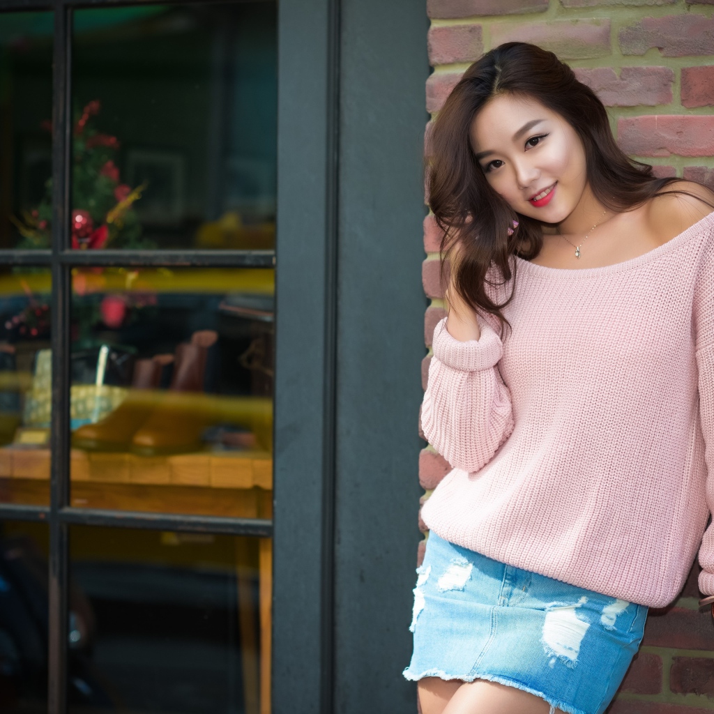 Милая азиатка в розовом свитере стоит у стены 