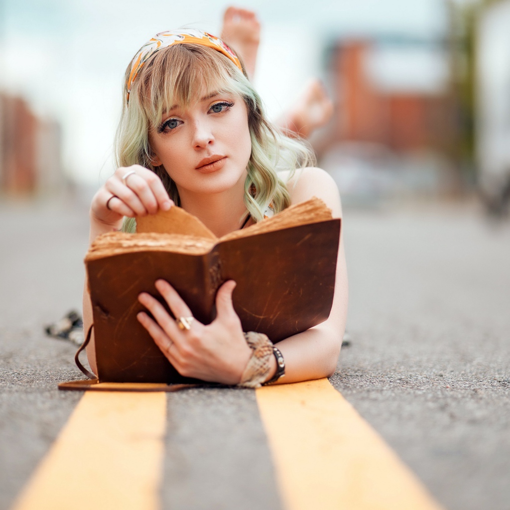 Милая блондинка лежит на асфальте с книгой 