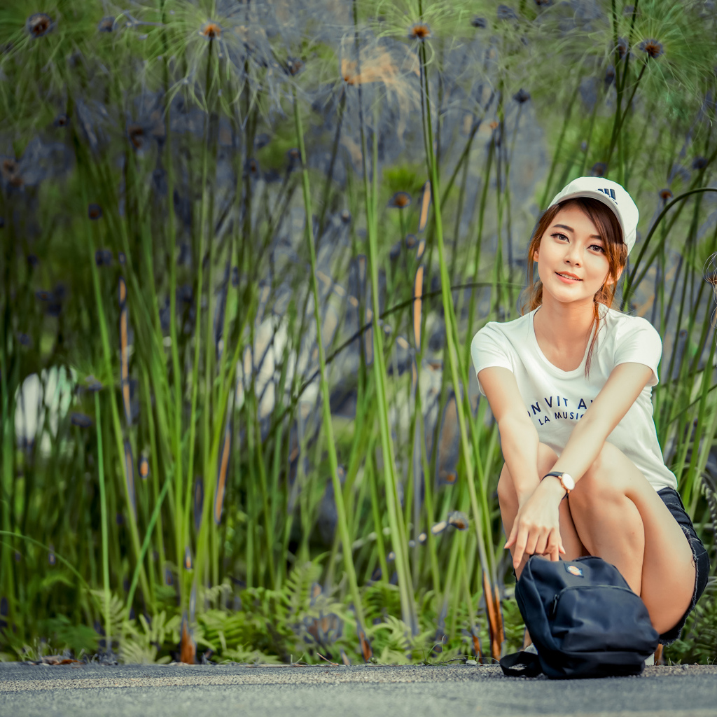 Милая девушка в кепке сидит на дороге с рюкзаком