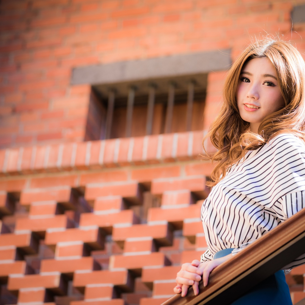 Милая девушка в полосатой рубашке стоит на ступеньках 