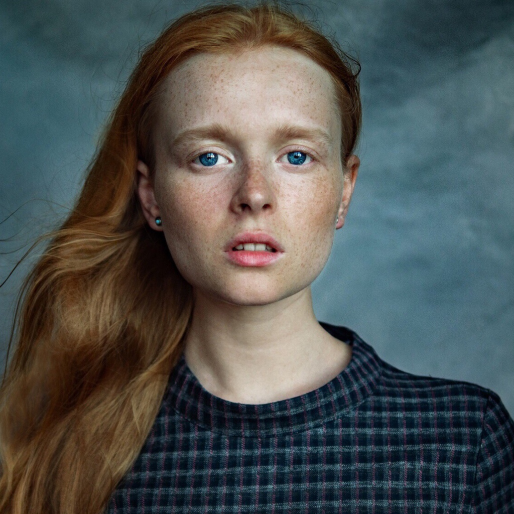 Милая рыжеволосая голубоглазая девушка с веснушками на лице на сером фоне