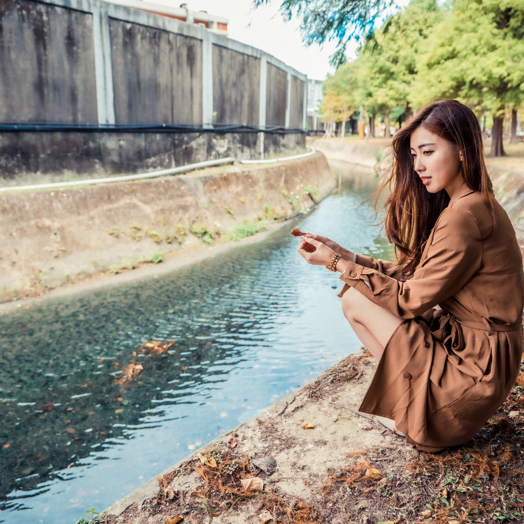 Мечтательная девушка азиатка сидит у воды