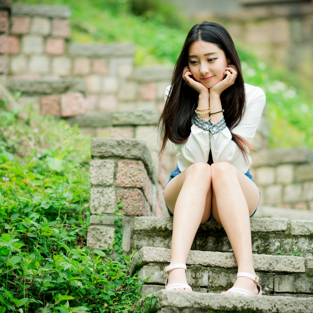 Мечтательная девушка азиатка сидит на ступеньках 