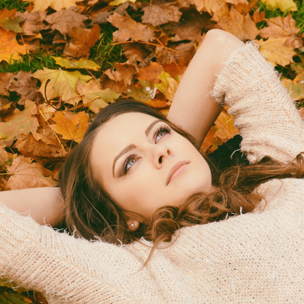 Мечтательная девушка в свитере лежит на земле
