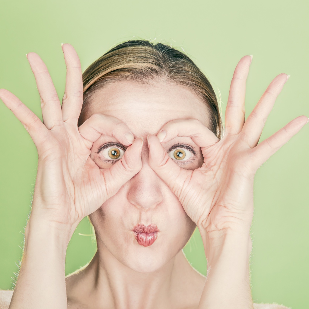 Смешная девушка делает руками очки на лице