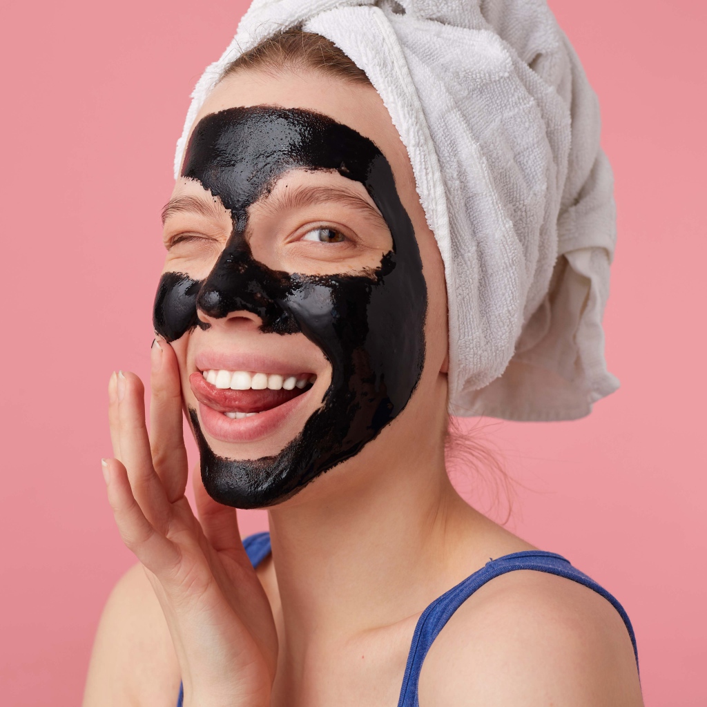 Смешная молодая девушка с черной косметической маской на лице 