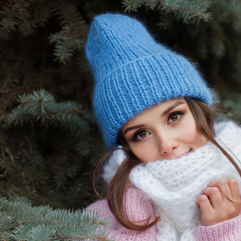Девушка в голубой вязаной шапке у ели