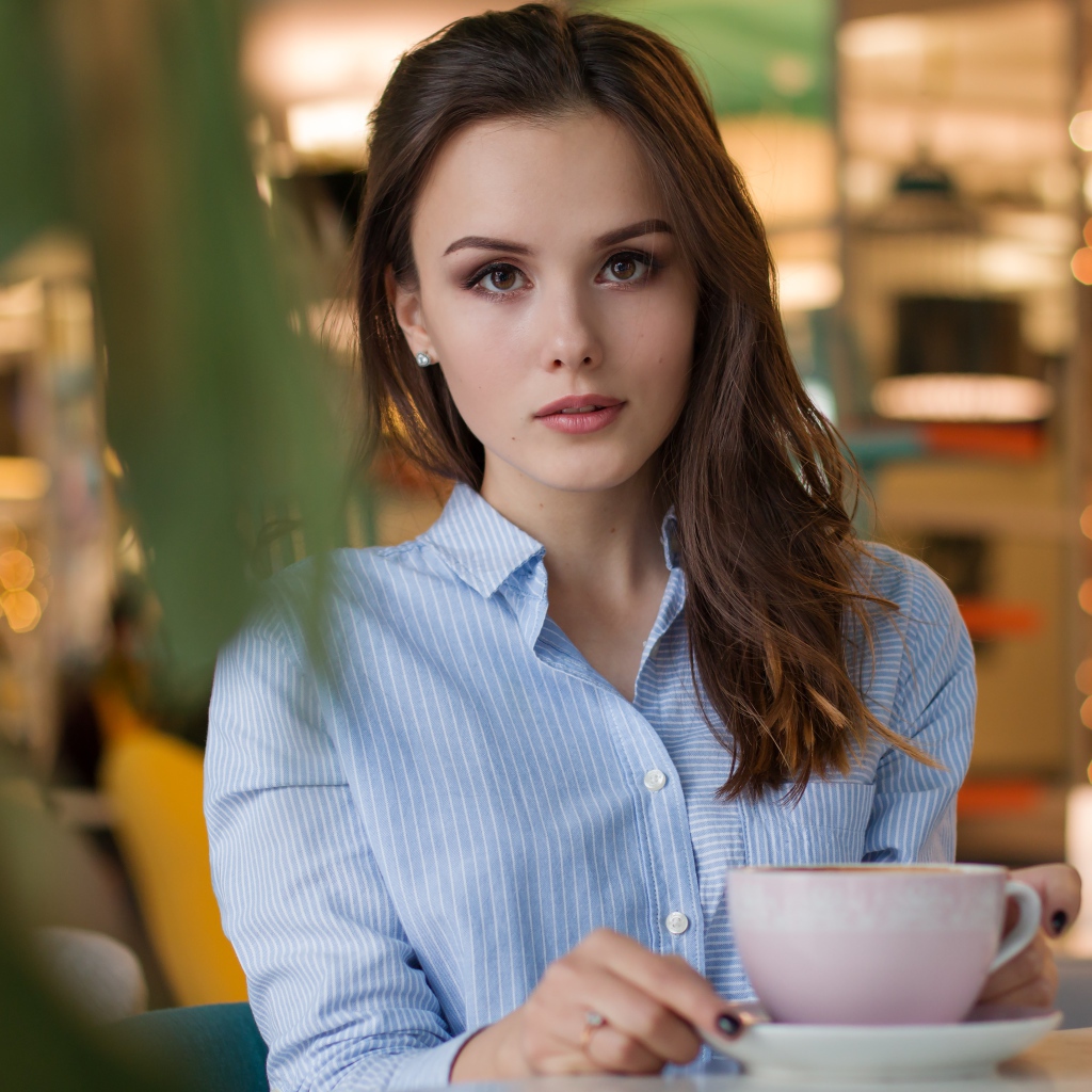 Девушка в голубой рубашке с чашкой кофе на столе в кафе