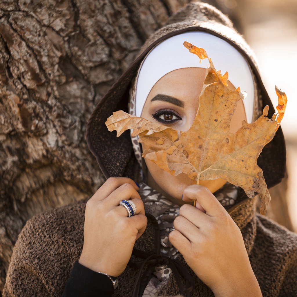 Девушка в пальто с закрывает лицо листом