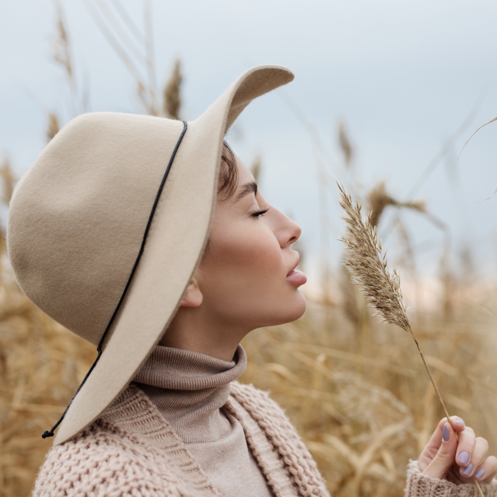 Девушка в шляпе с закрытыми глазами держит колосок 