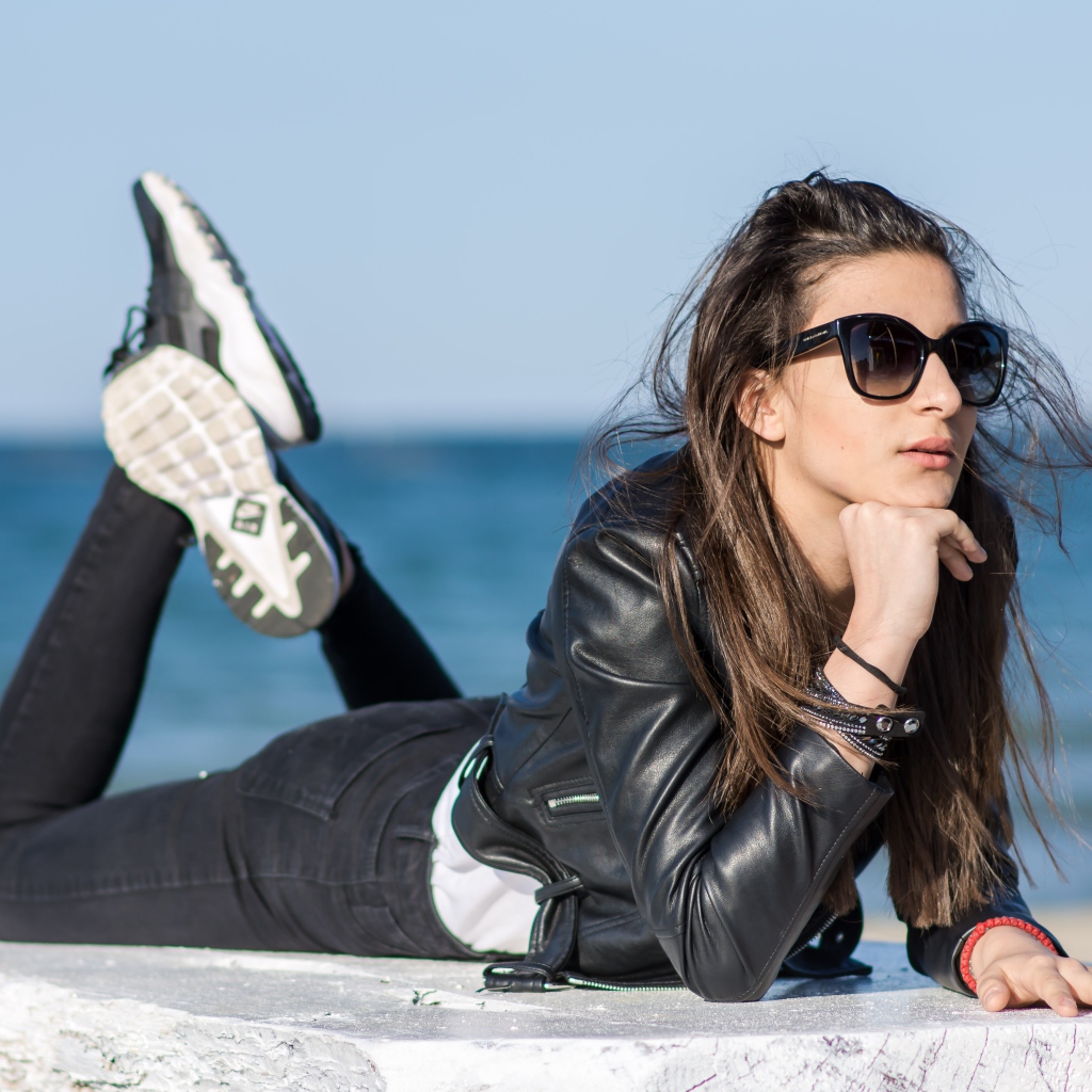 Девушка в черных очках и кожаной куртке на фоне моря