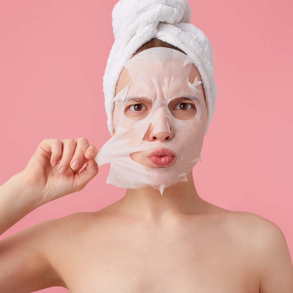 Девушка снимает косметическую маску с лица на розовом фоне 