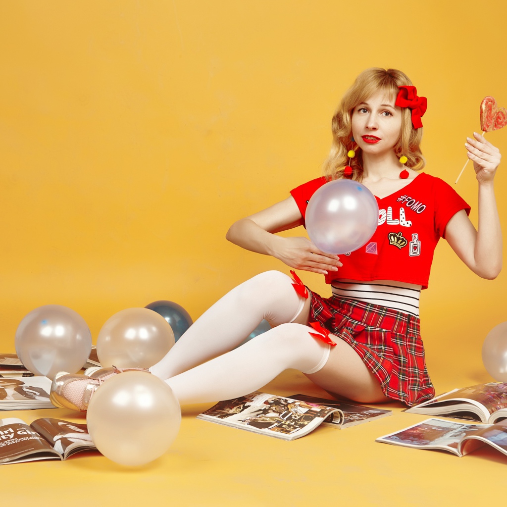 Девушка с шариками и журналами сидит на полу