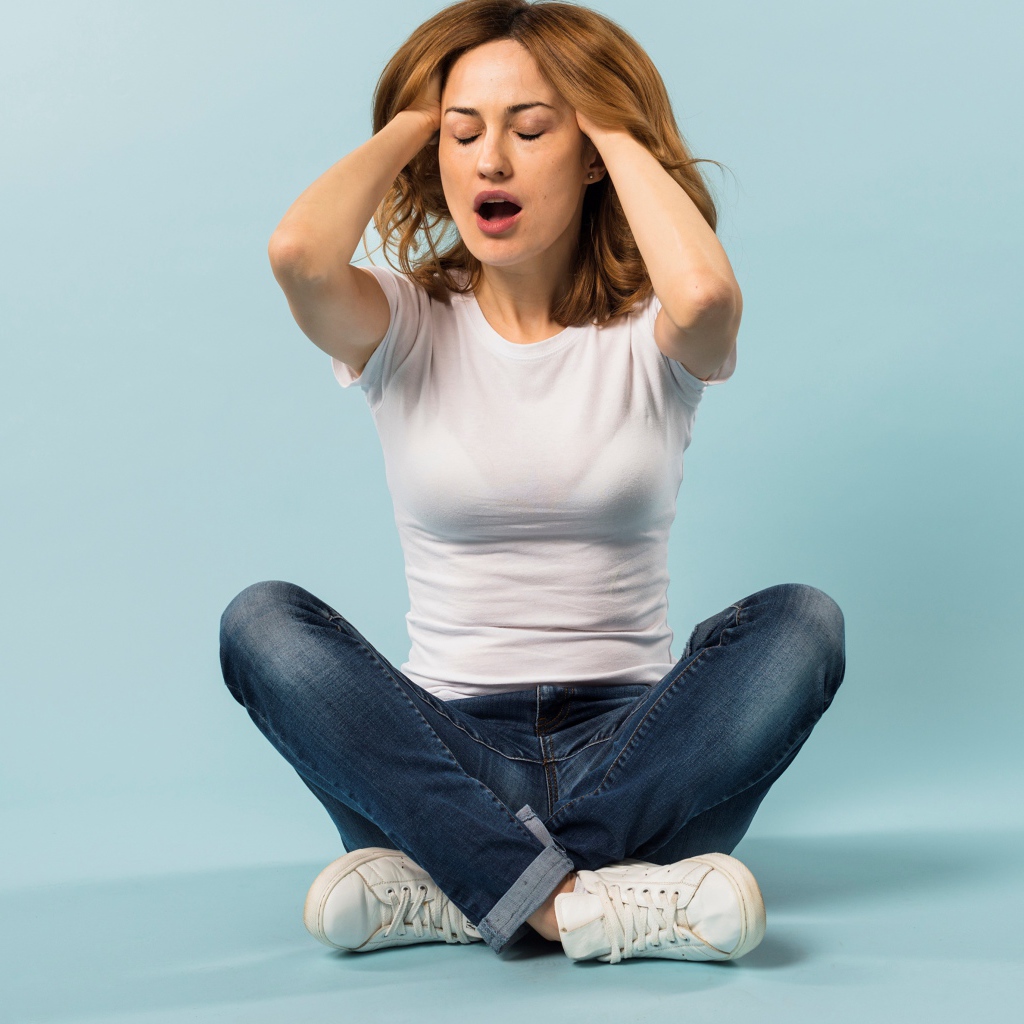 Девушка с руками в волосах сидит в джинсах на голубом фоне