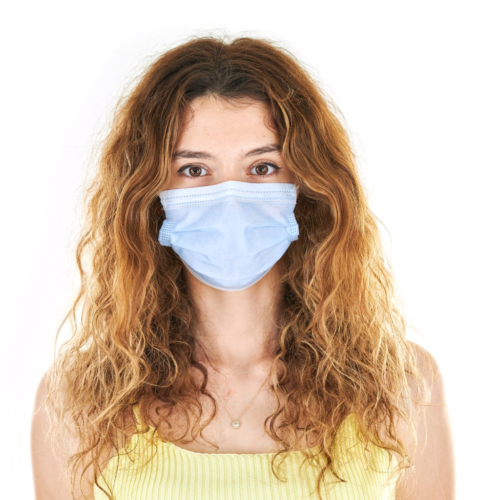 Длинноволосая девушка в маске от коронавируса на белом фоне