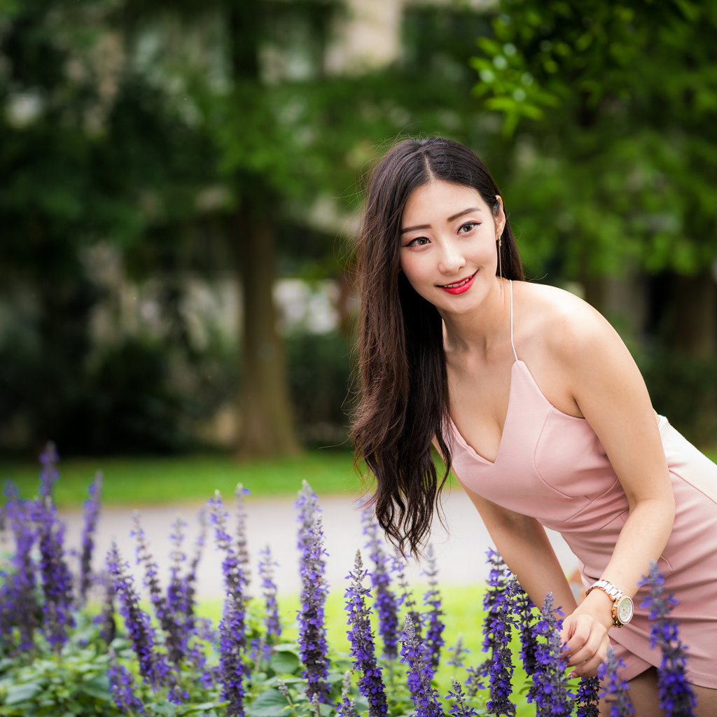 Милая девушка Азиатка в розовом платье у синих цветов