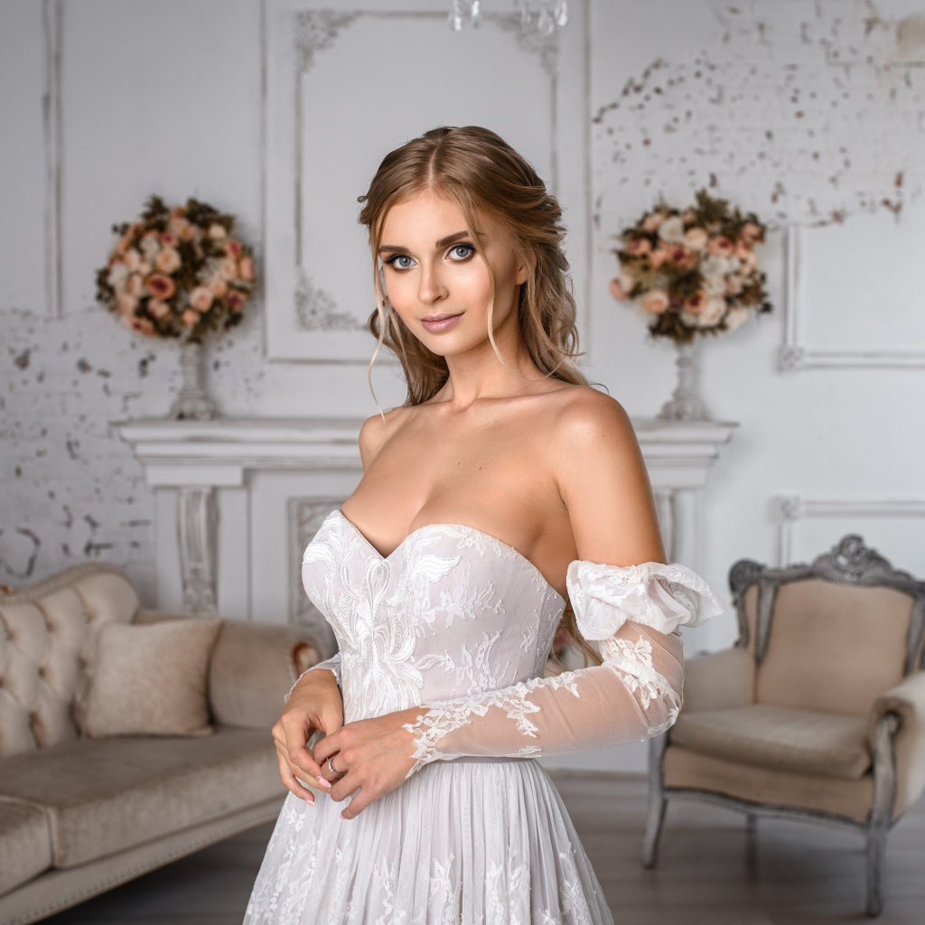 Милая девушка в свадебном платье в комнате с диваном