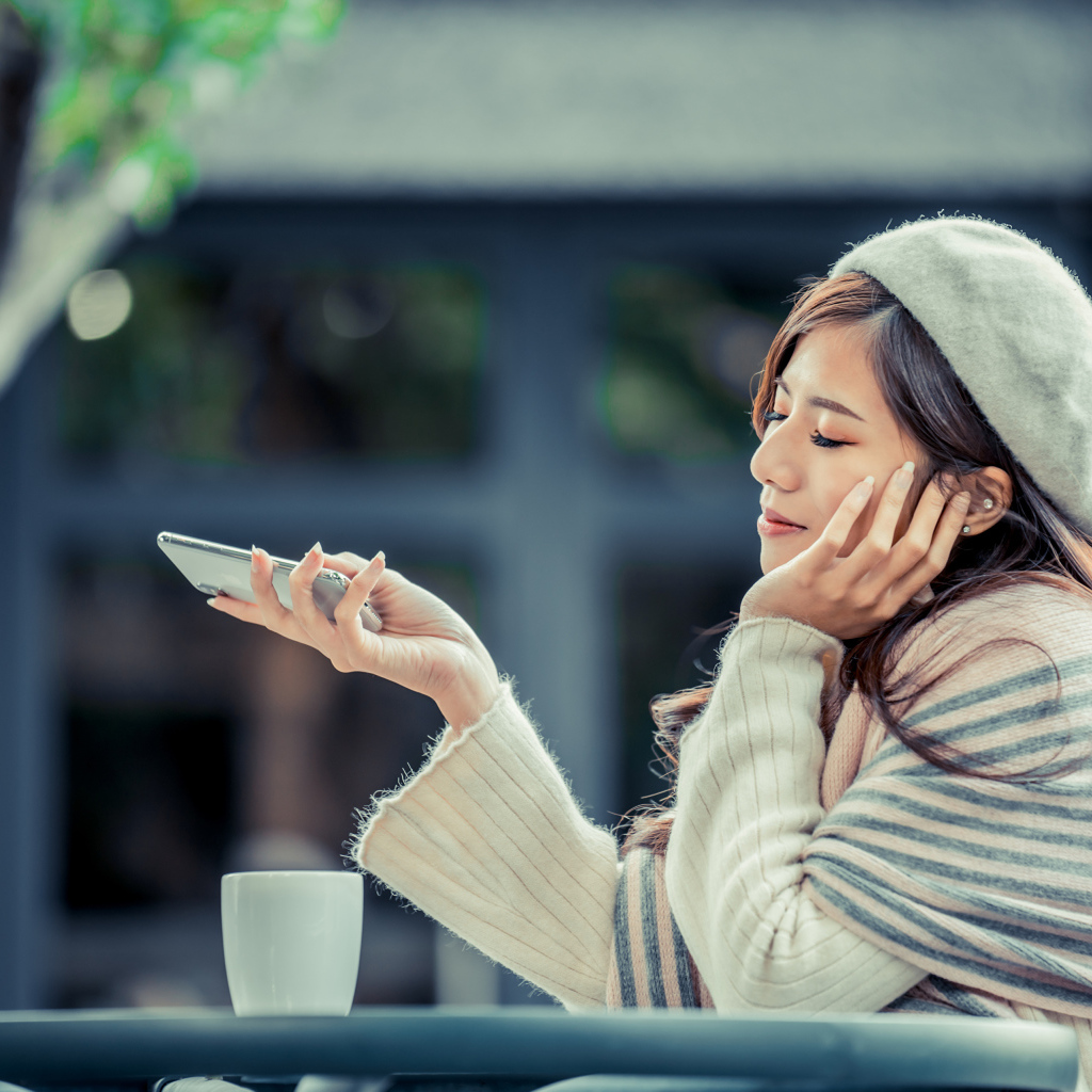 Мечтательная девушка с телефоном сидит в кафе 