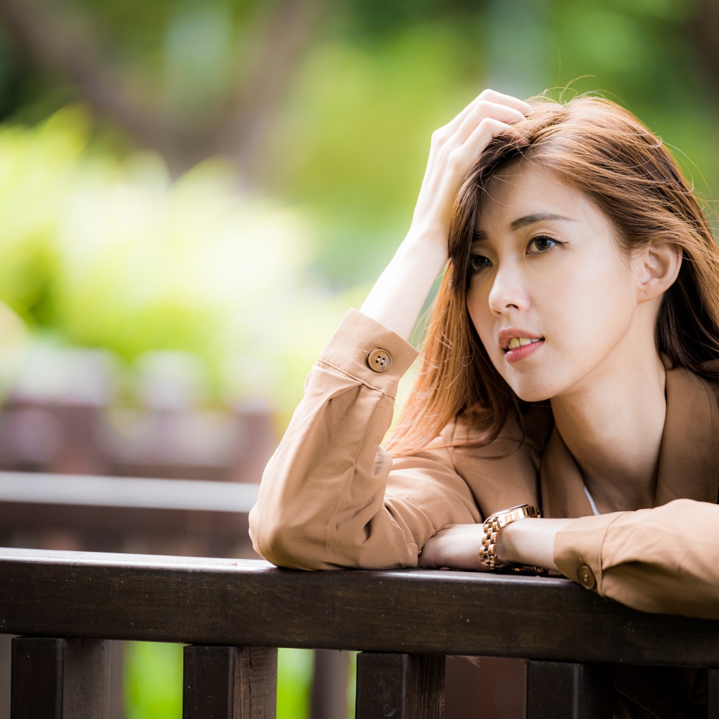 Грустная девушка азиатка стоит у деревянных перил 