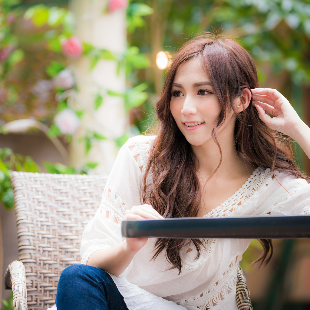 Улыбающаяся девушка азиатка сидит за столом в кафе