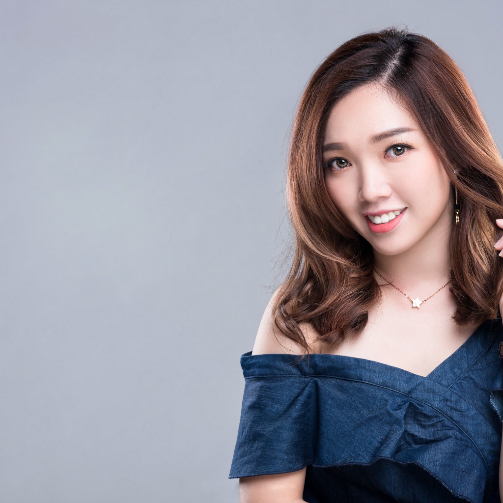 Улыбающаяся девушка азиатка с часами на руке на сером фоне